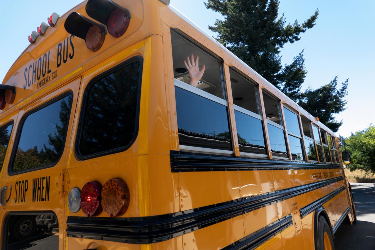 A student waves as the school bus leaves Kneeland Elementary School in August 2022.