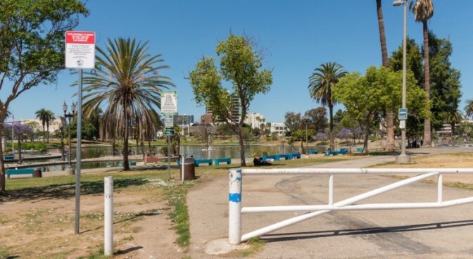 A red and white sign is posted at a roadway entrance into a park with a body of water and trees in the background.