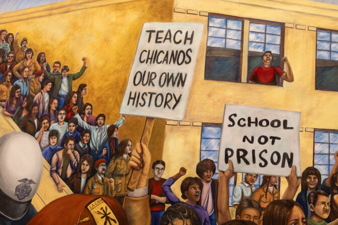 A mural depicts crowds of people protesting outside a yellow multi-story building.