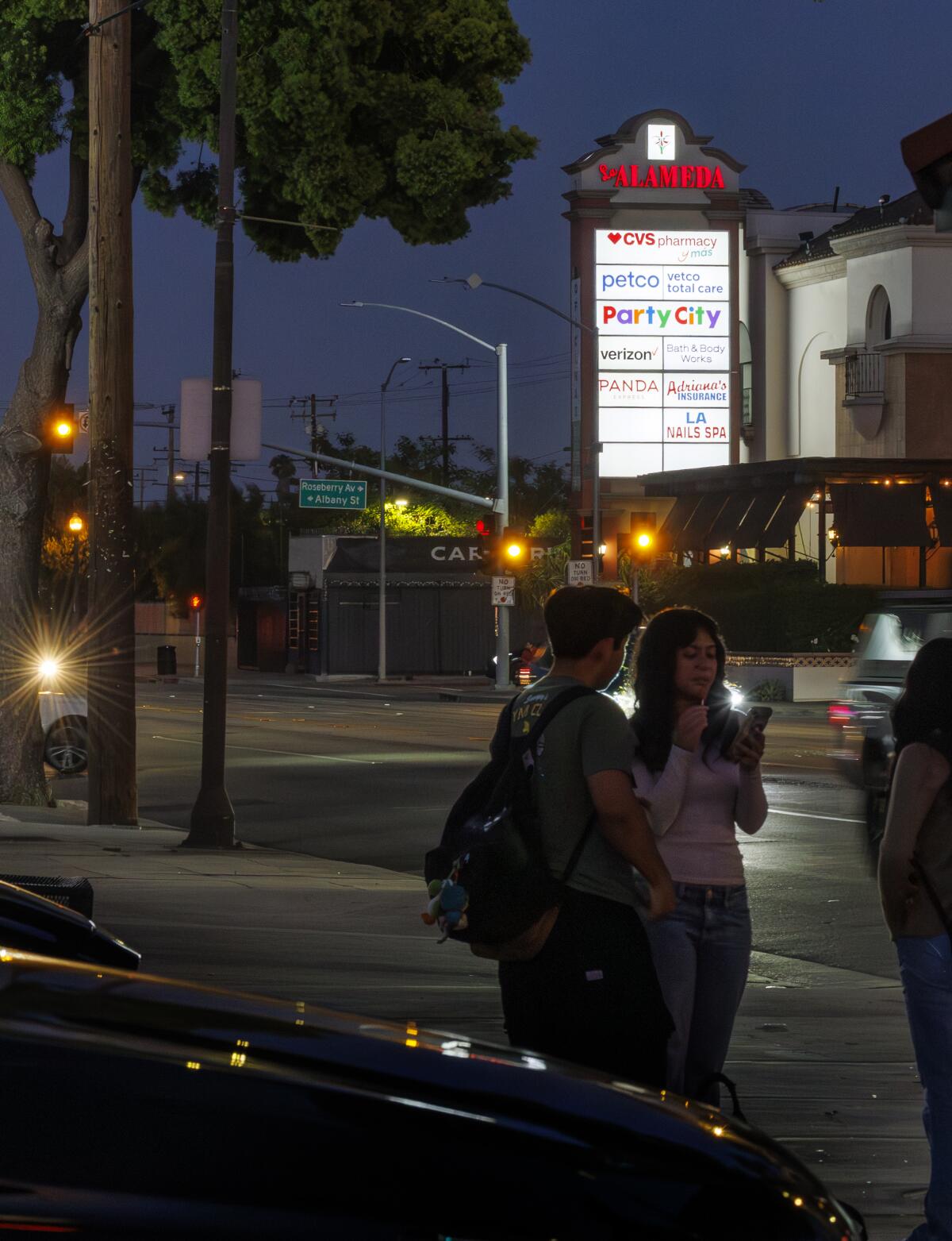 Residents wait at a bus stop across from at Plaza La Alameda in Walnut Park.