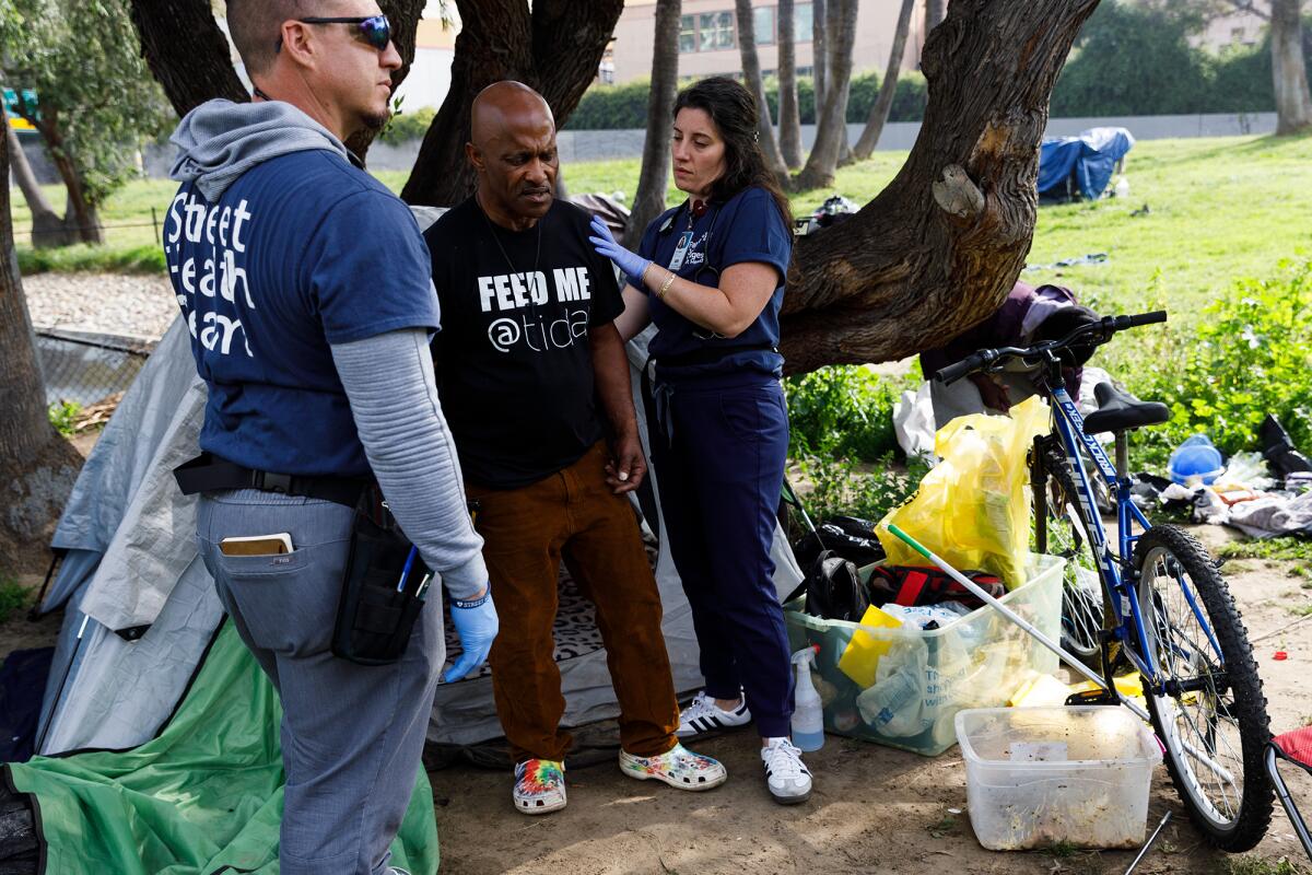 Two people examine a man in an encampment in downtown San Diego.