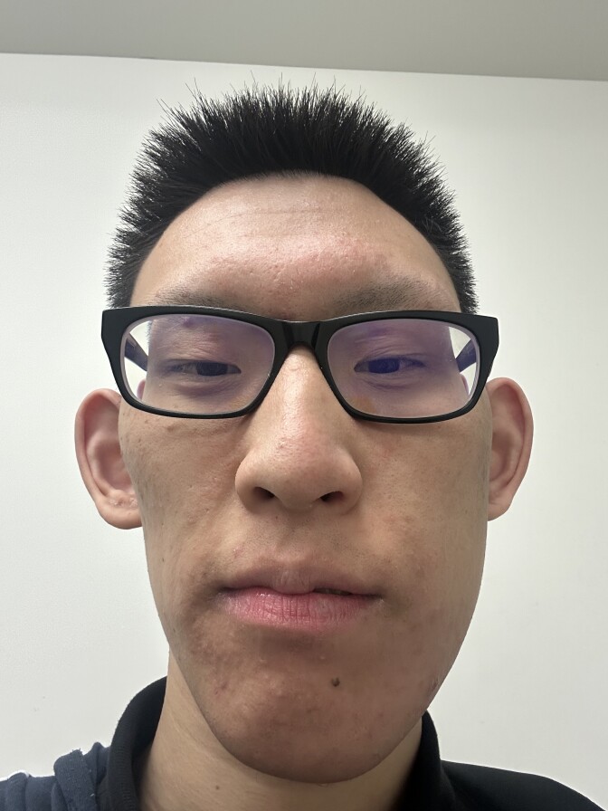 A man with medium skin tone, dark hair and glasses looks at the camera.