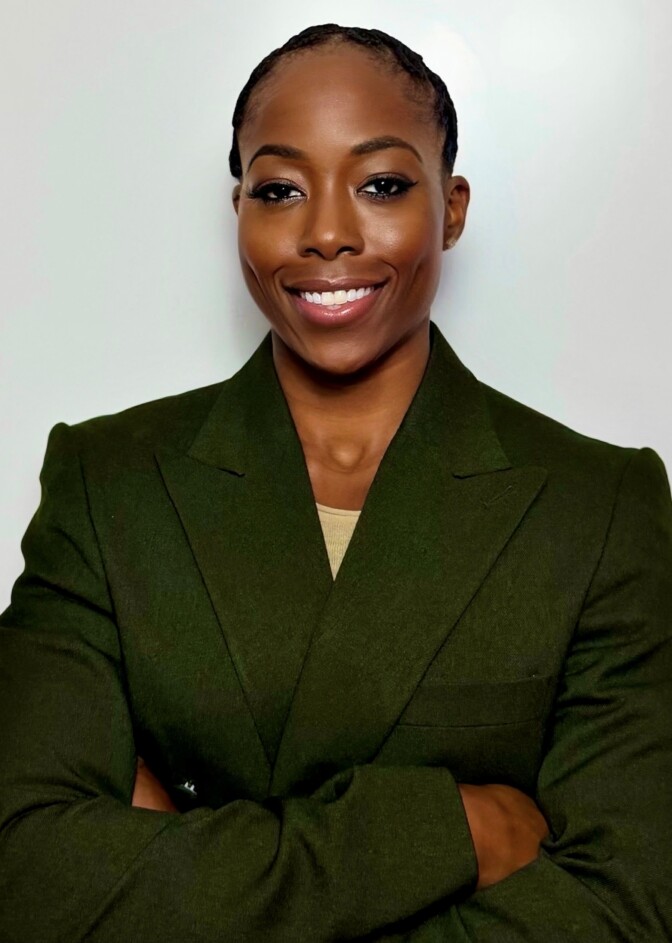 A woman with dark skin tone crosses her arms and smiles.