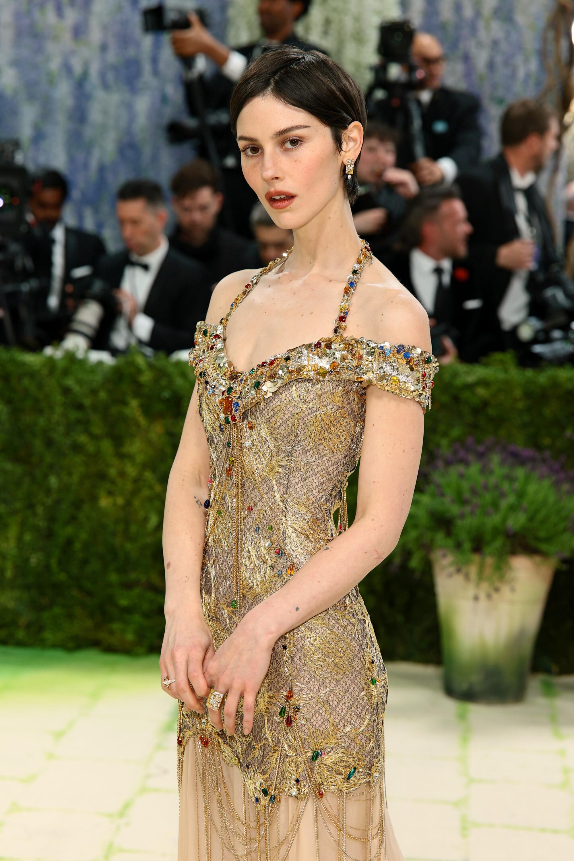 Gracie Abrams, wearing a gold dress, poses at the Met Gala. 