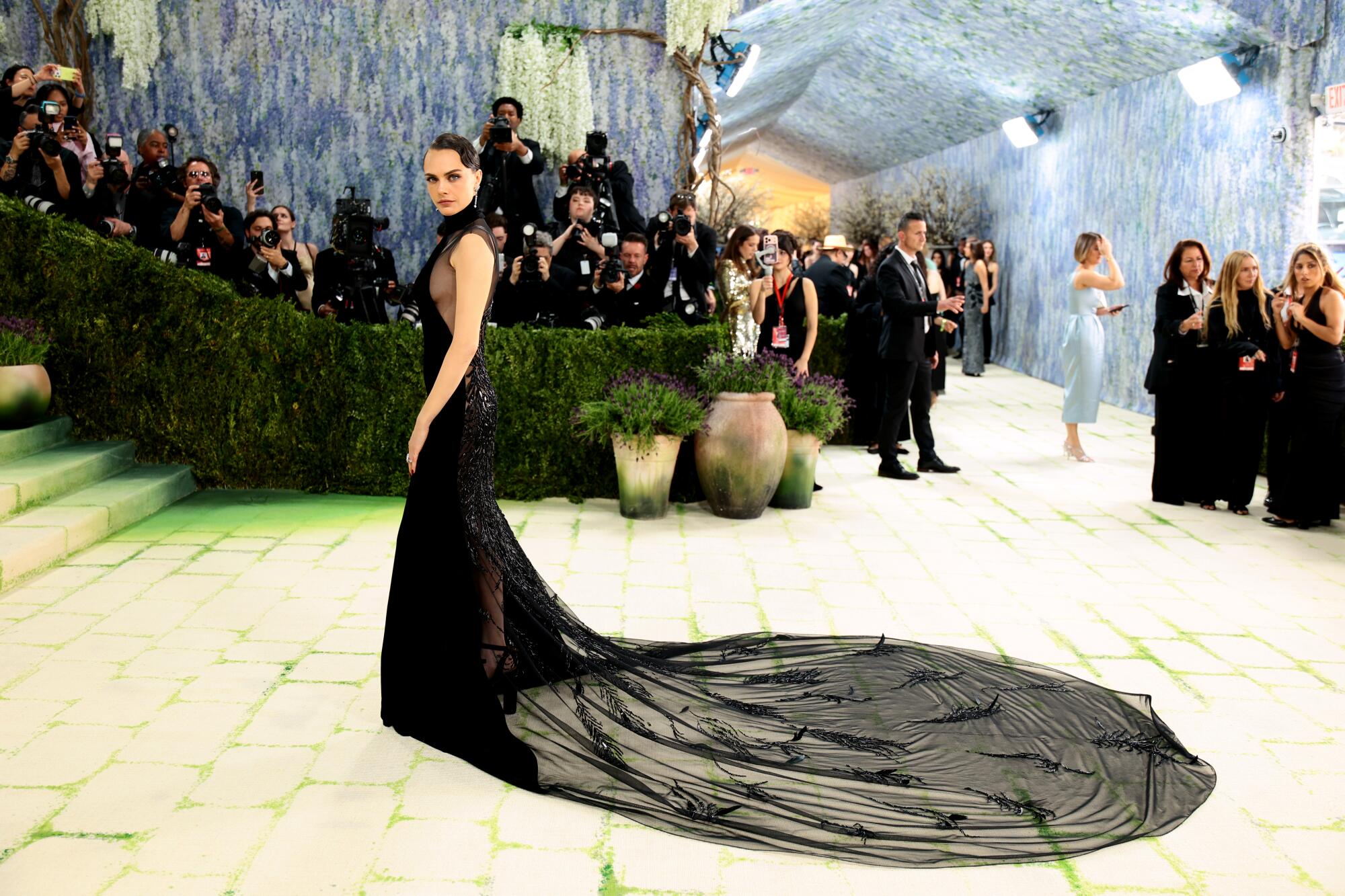 Cara Delevingne, wearing a black gown with a long train, poses at the Met Gala. 