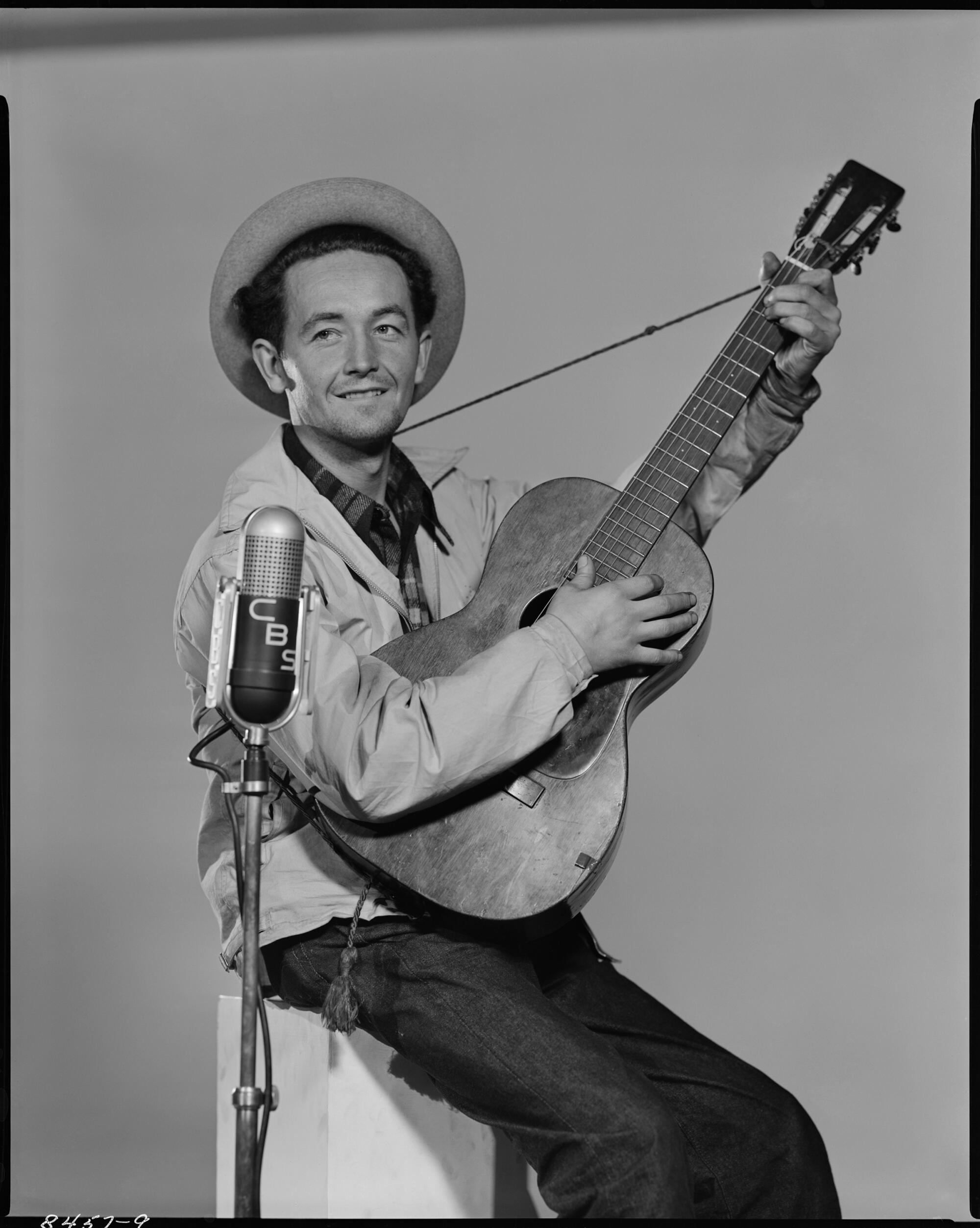 Woody Guthrie seated and holding a guitar