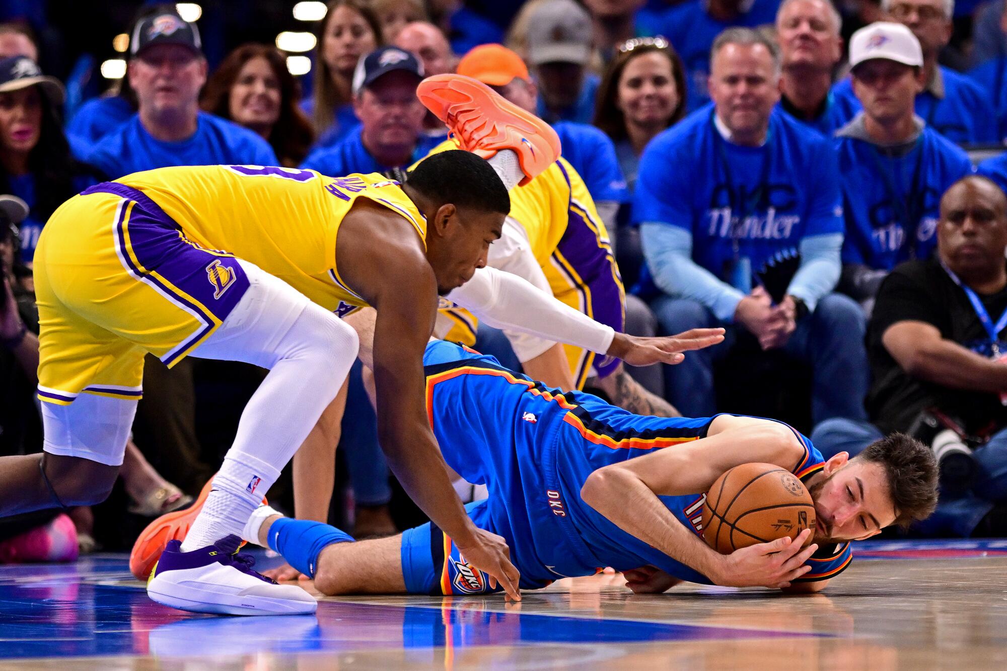 Thunder center Chet Holmgren, lying on the court, grabs a loose ball before Lakers forward Rui Hachimura can during Game 1