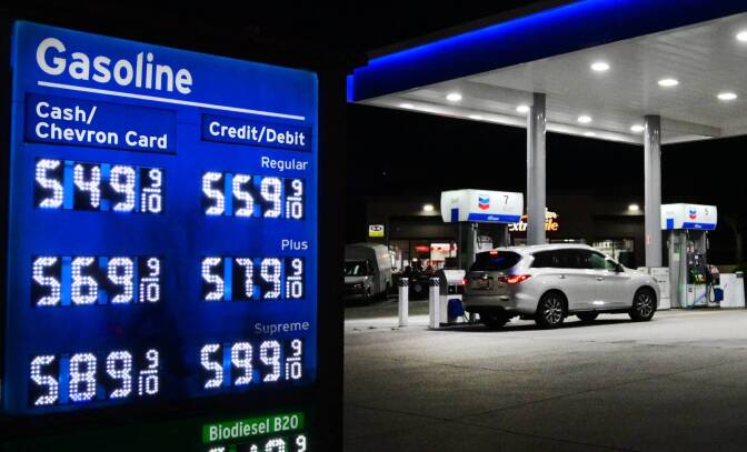 A gas station with blue signage showing gas prices ranging from 5.49 to 5.89 with cash. A car is parked at a pump at night in the background.