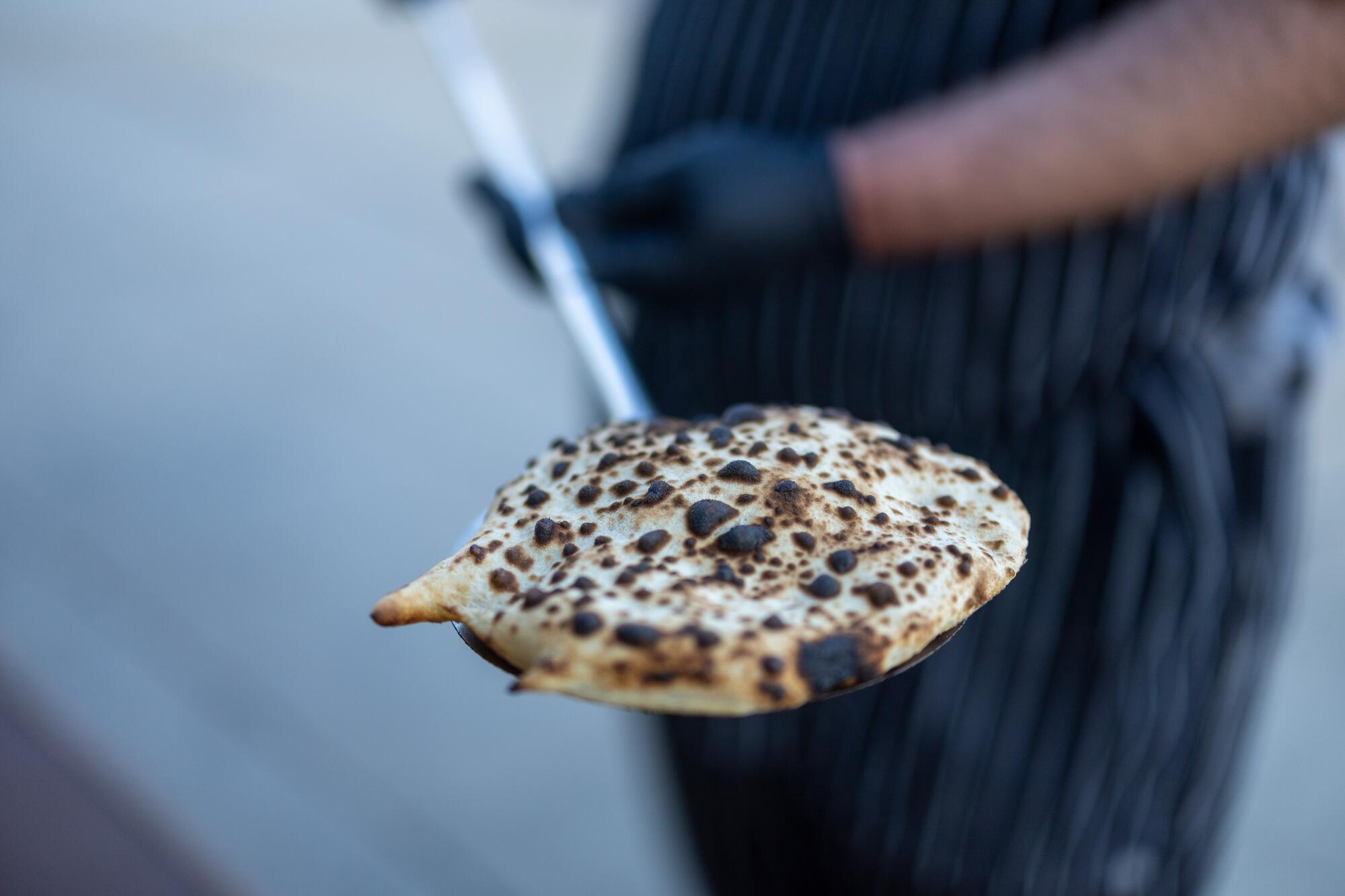 Chef-owner Arthur Grigoryan takes a puffy, char-spotted pita out of his outdoor stove at Yerord Mas in Glendale.