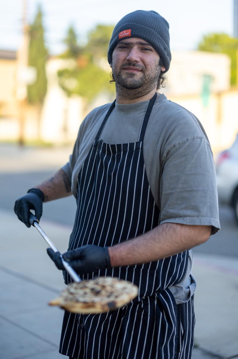 GLENDALE, CA - APRIL 30, 2026: Chef-owner Arthur Grigoryan holding a piece of bread freshly pulled out of an outdoor stove at Yerord Mas on Thursday, April 30, 2026 in Glendale, CA. (Ronaldo Bolanos / Los Angeles Times)