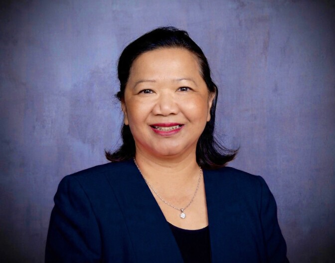 a smiling woman with shoulder length dark hair wears a blue blazer and a black blouse with a necklace
