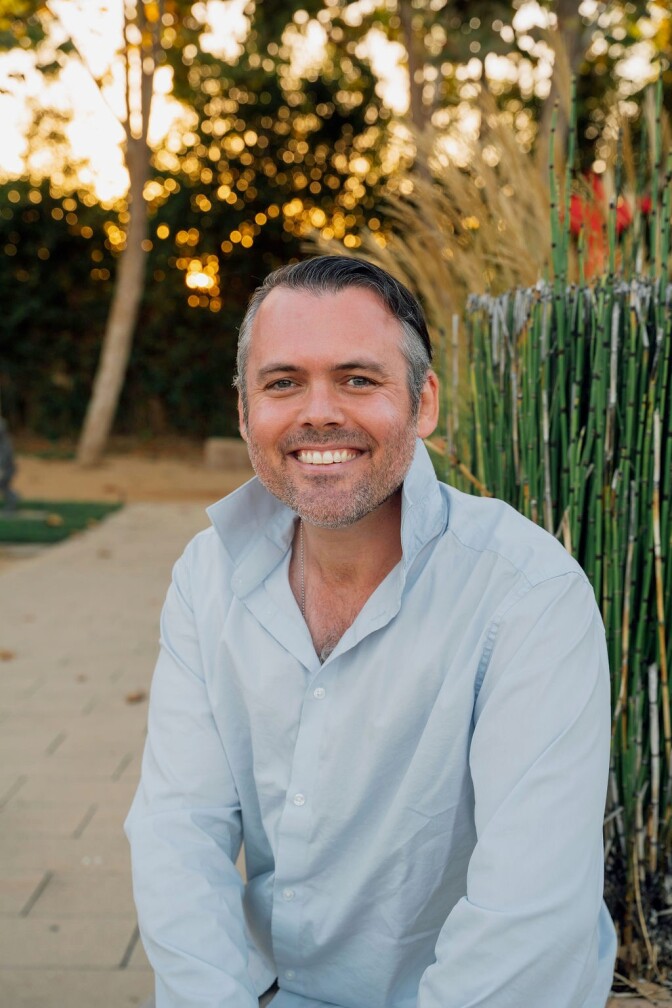 a smiling man with short salt and pepper hair wearing a light blue collared button up