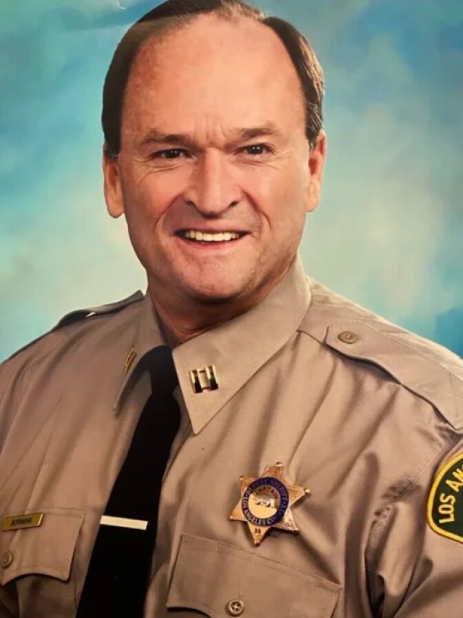 a smiling man with short brown hair in a law enforcement uniform with a badge on his chest