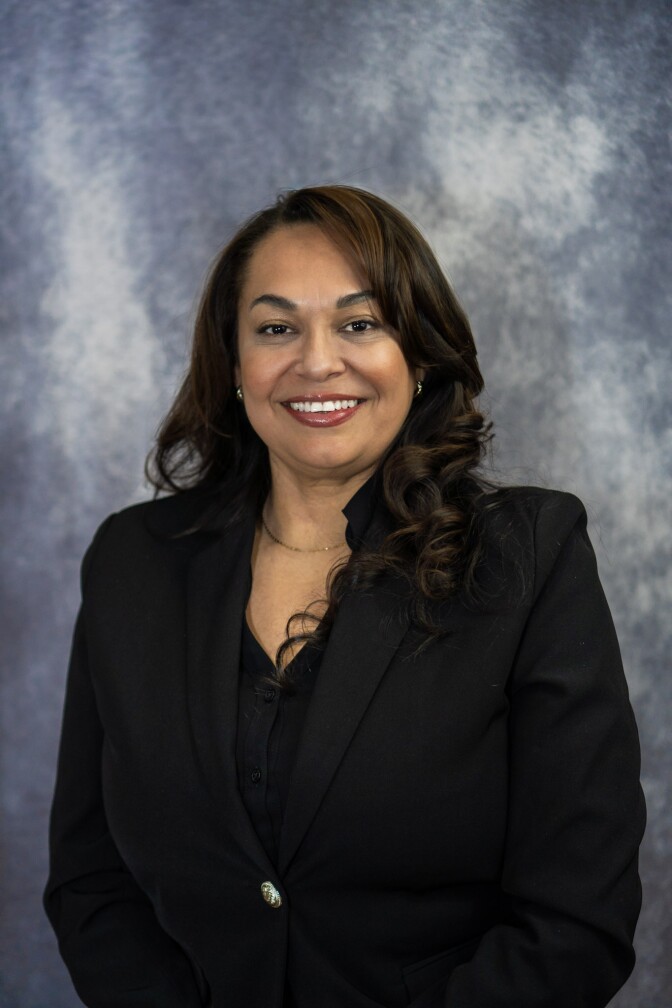 a smiling woman with long dark hair with a black blazer and black blouse