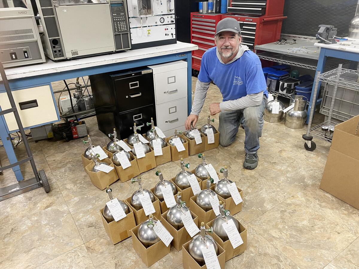 Tim Nelligan kneels next to multiple small cardboard boxes containing metal device with tags.