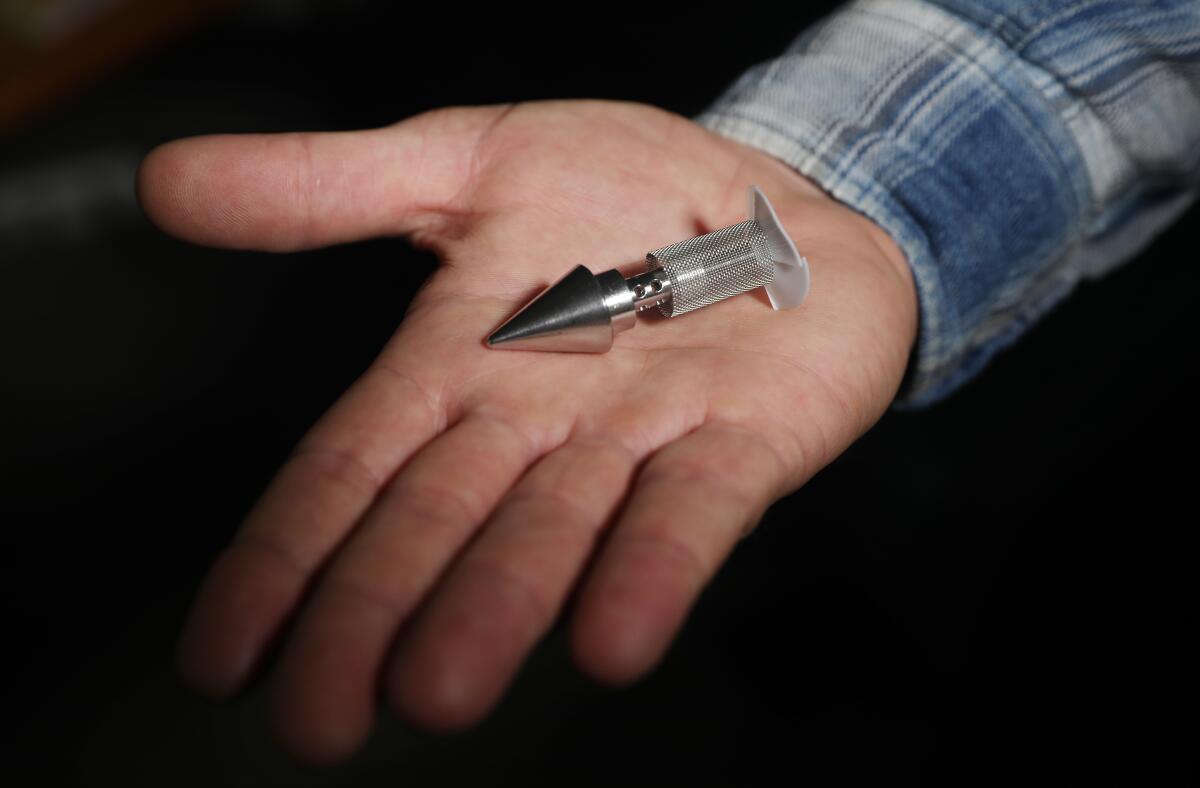 A probe with a silver metal point on one end, held in the open palm of an outstretched hand