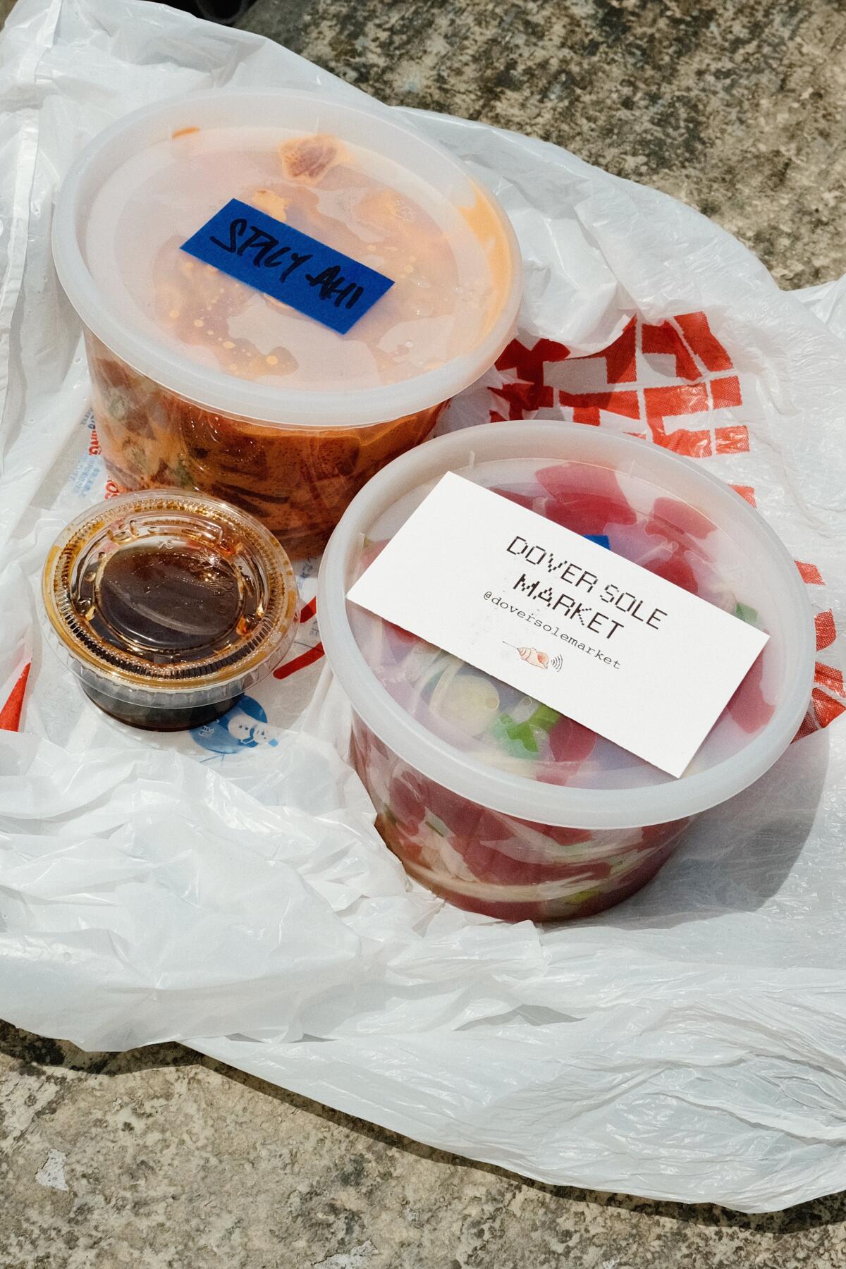 Plastic containers of ahi tuna with onion and spicy tuna on a plastic bag with a side of shoyu