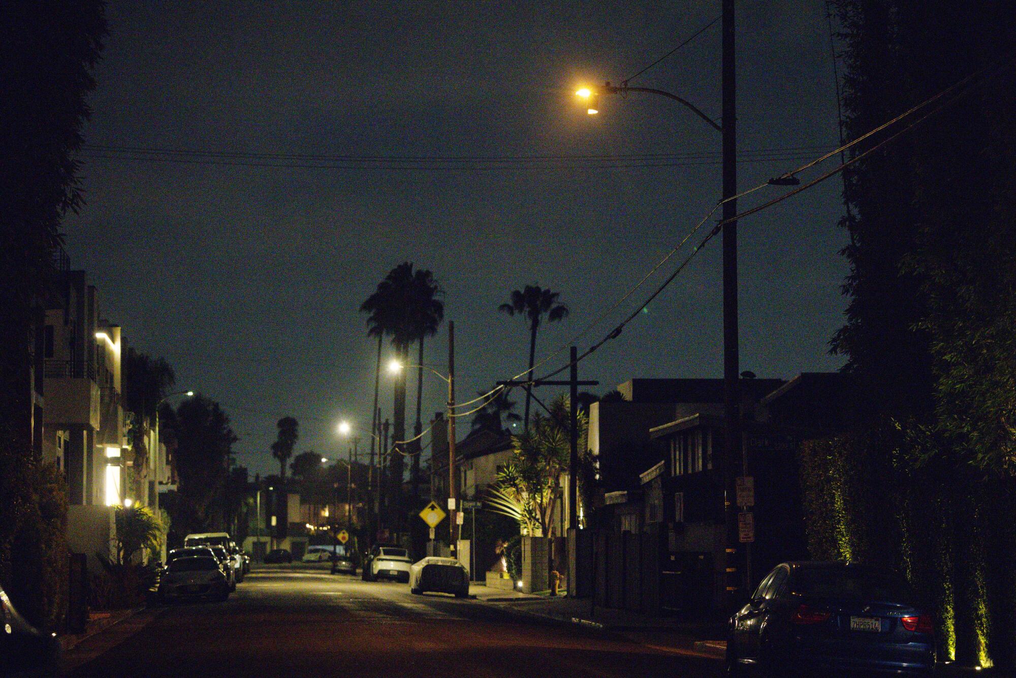 An orange streetlight among the new LED lights on a street lined with buildings and some palm trees