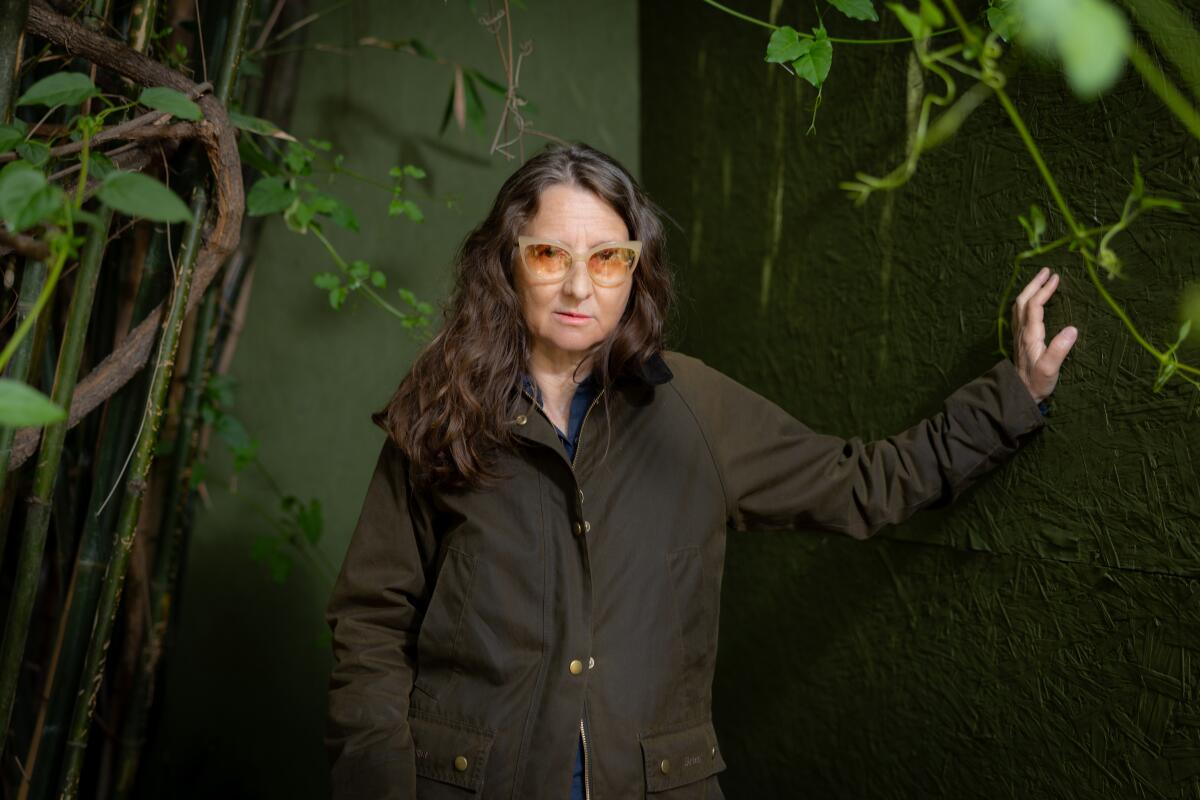 A woman stands in front of a leafy backdrop.