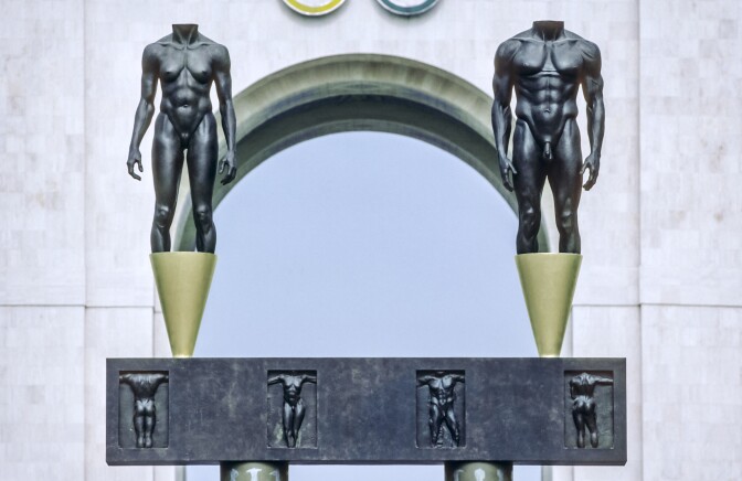 A closeup of two nude statues that stand outside an archway.