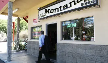 A person, wearing a blue-and-white striped shirt and black pants, walks past a building with a sign that reads "Montana Bail Bonds."