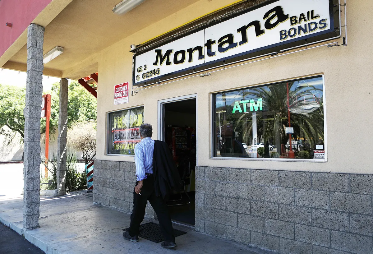 A person, wearing a blue-and-white striped shirt and black pants, walks past a building with a sign that reads "Montana Bail Bonds."