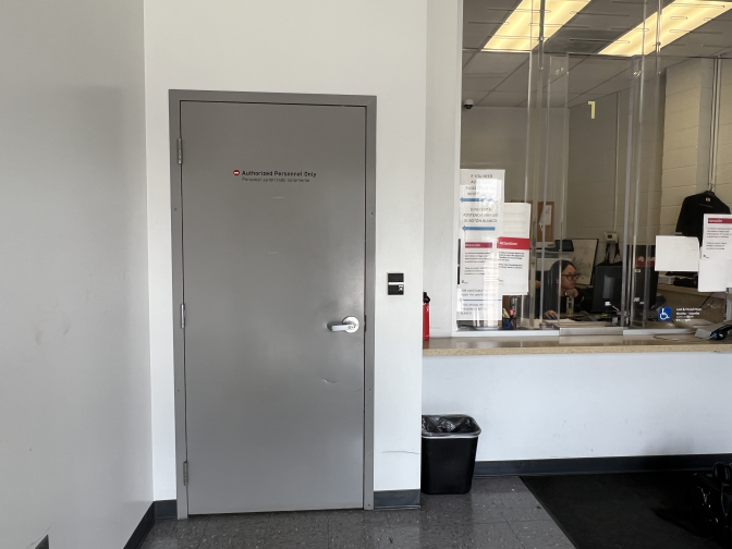 A gray door is seen in a room it has the words "Authorized Personnel Only" on it. There's a concierge desk behind a glass barrier to the left of the door.