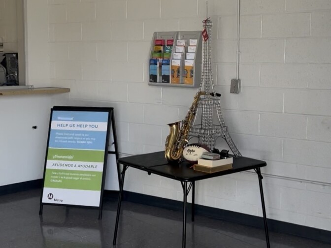 A small black table is seen in a room with a small eiffel tower, a saxophone, a football, black sunglasses, a wallet and some books on top of it.