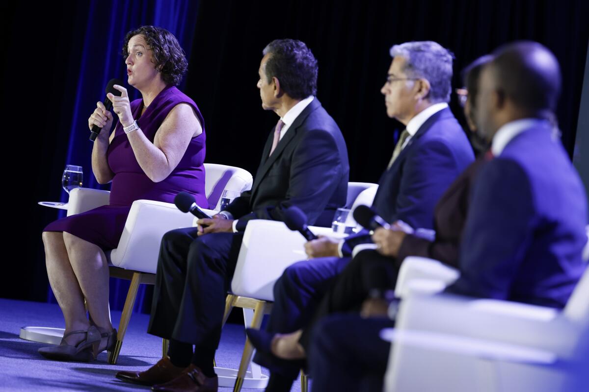 Katie Porter, left, speaks while seated onstage alongside other candidates