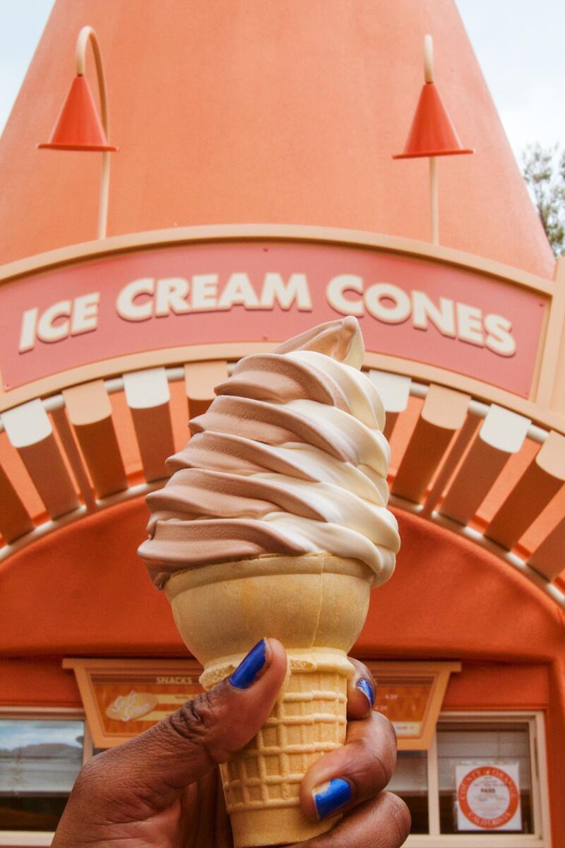 A hand holds up a chocolate and vanilla swirled soft serve cone in front of an orange cone-shaped stand