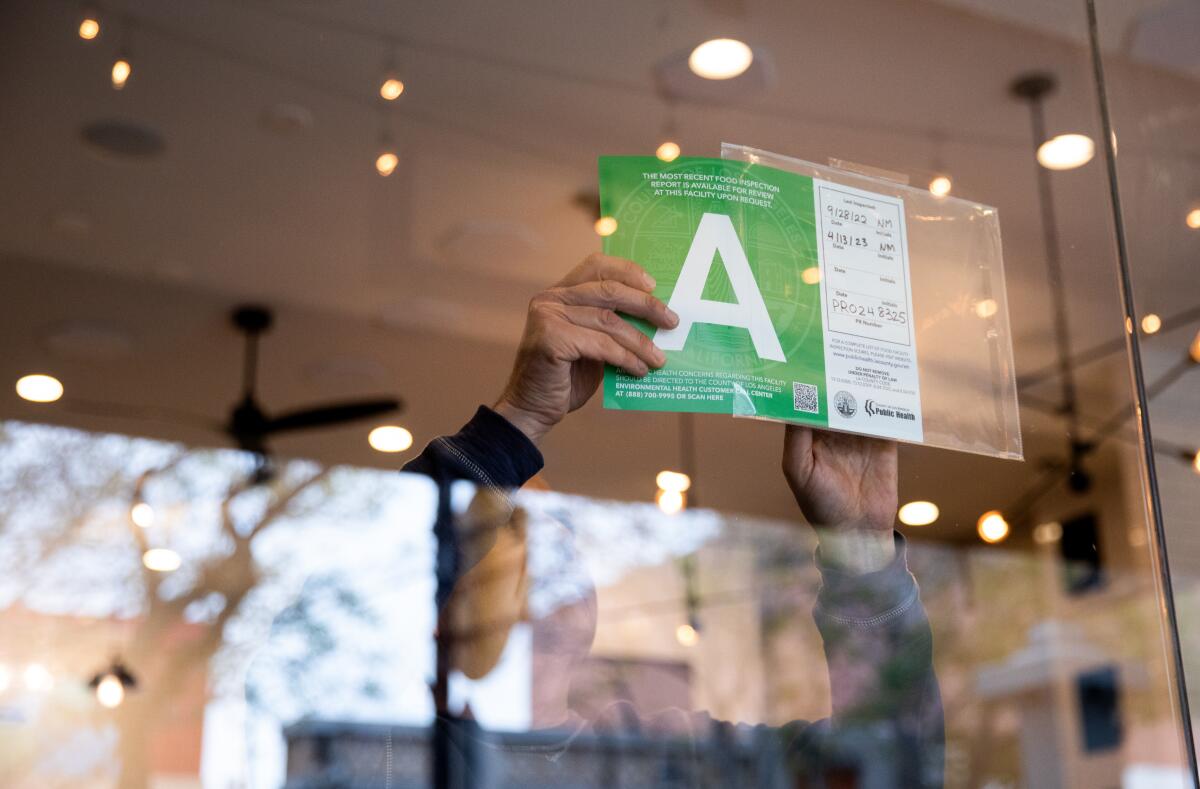 A Burbank restaurant owner puts his newly updated A health inspection score in the window in 2023.