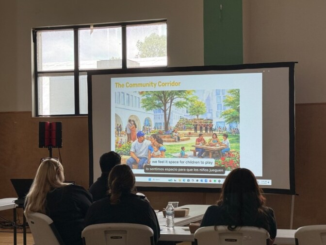 People sitting on chairs around a table look towards a screen projector displaying an illustration and text reading "The community corridor."