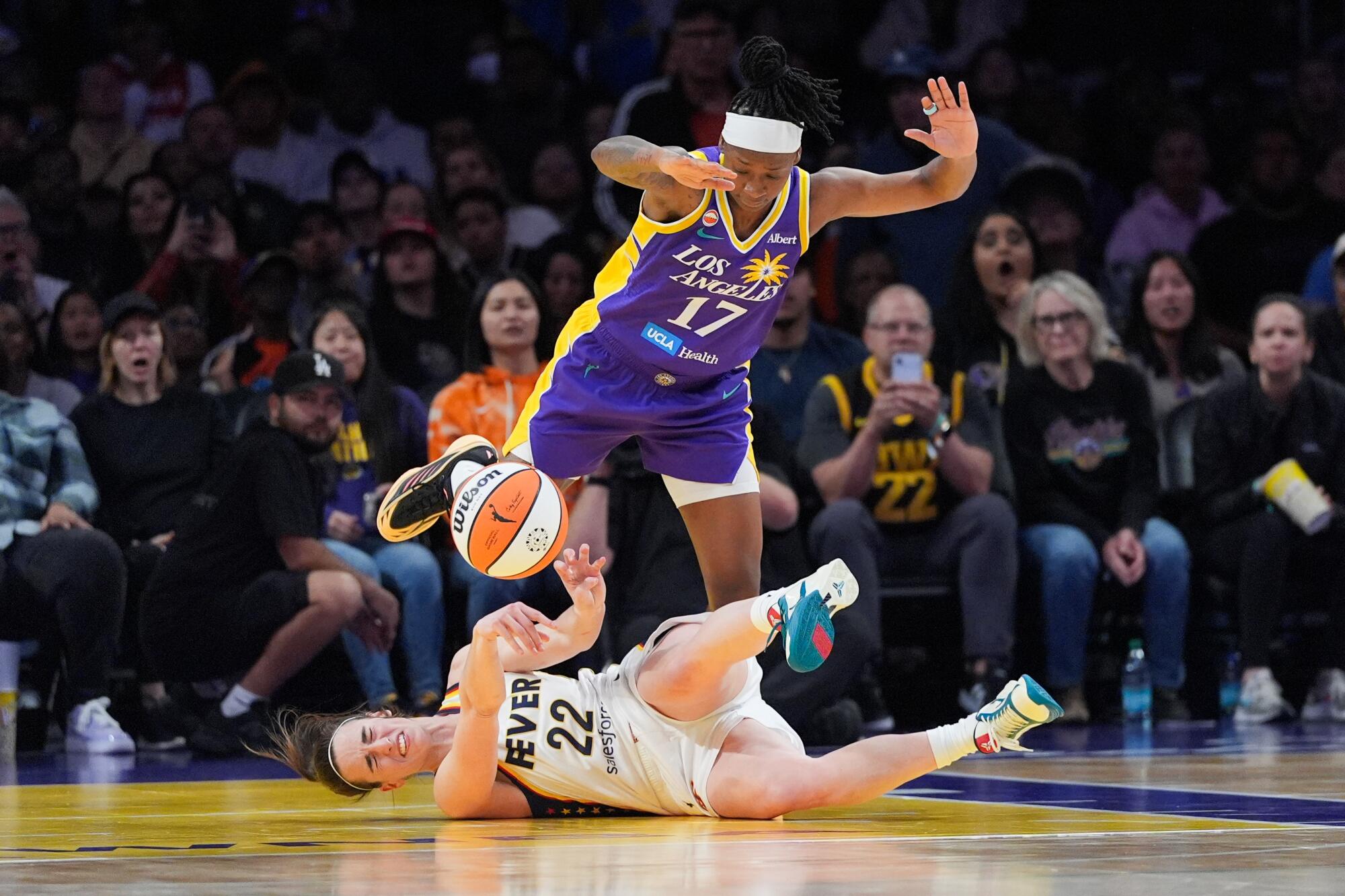 Fever guard Caitlin Clark attempts a pass while falling to the court Sparks guard Erica Wheeler steps around her.