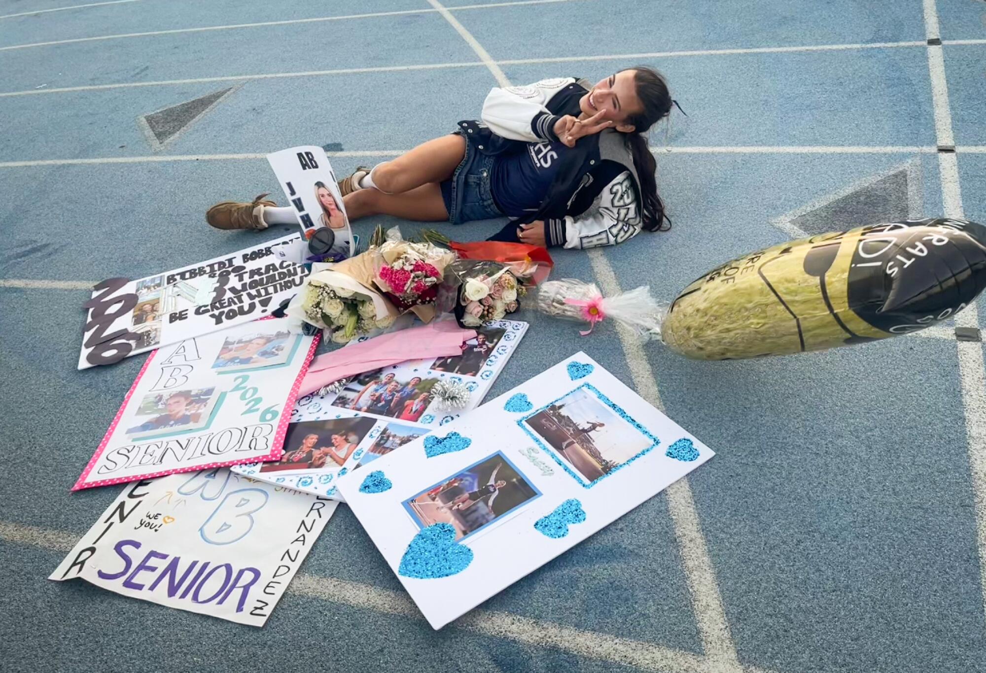 Jurupa Valley athlete AB Hernandez, who is transgender, poses on a track with senior day posters supporting her.