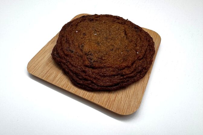 A close-up of a chocolate chip cookie lying on a small plate.