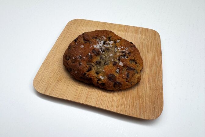 A close-up of a chocolate chip cookie lying on a small plate.