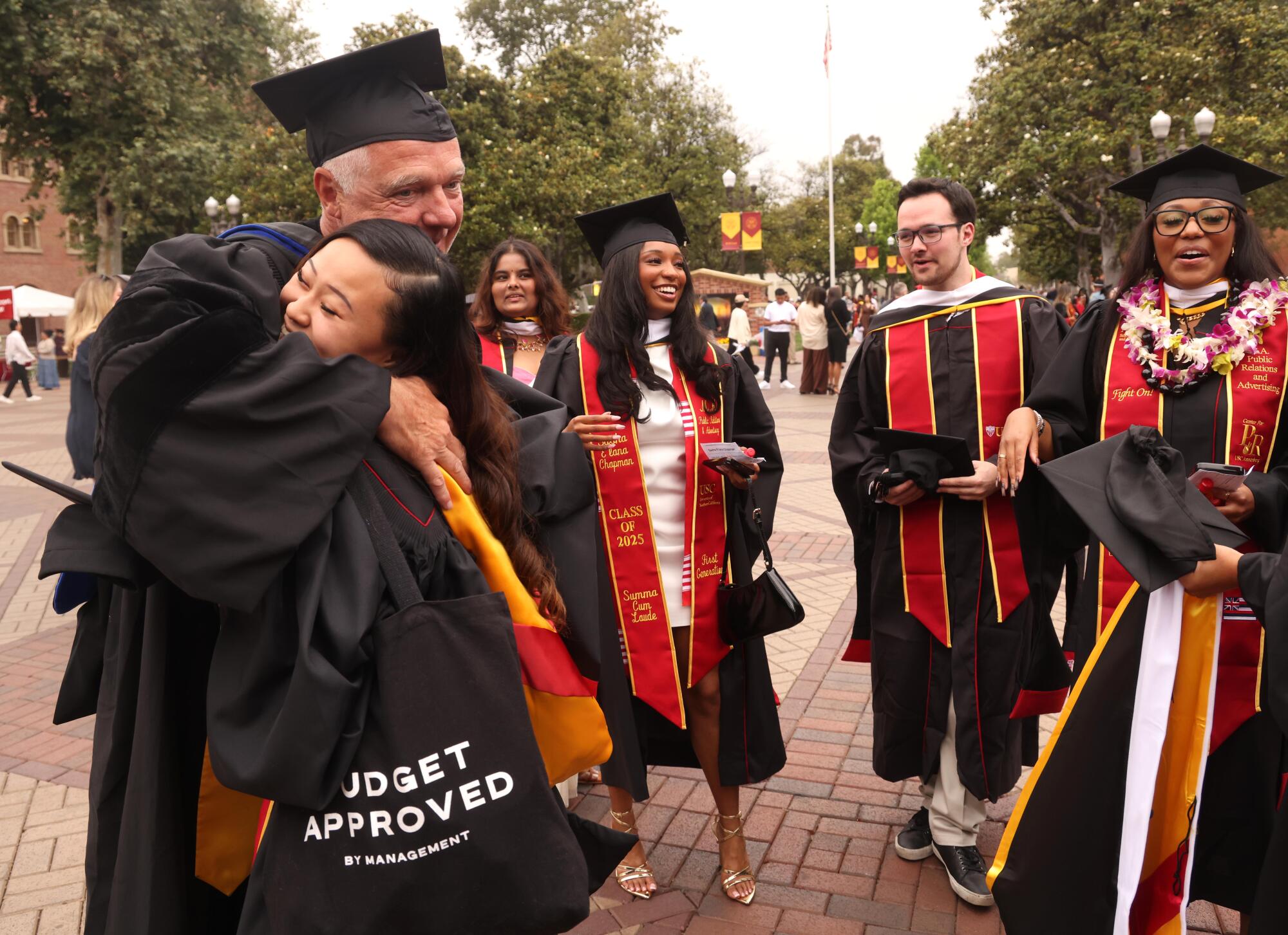 Jessica To, foreground, hugs her professor Burghardt Tenderich while other graduates look on at the commencement ceremony.