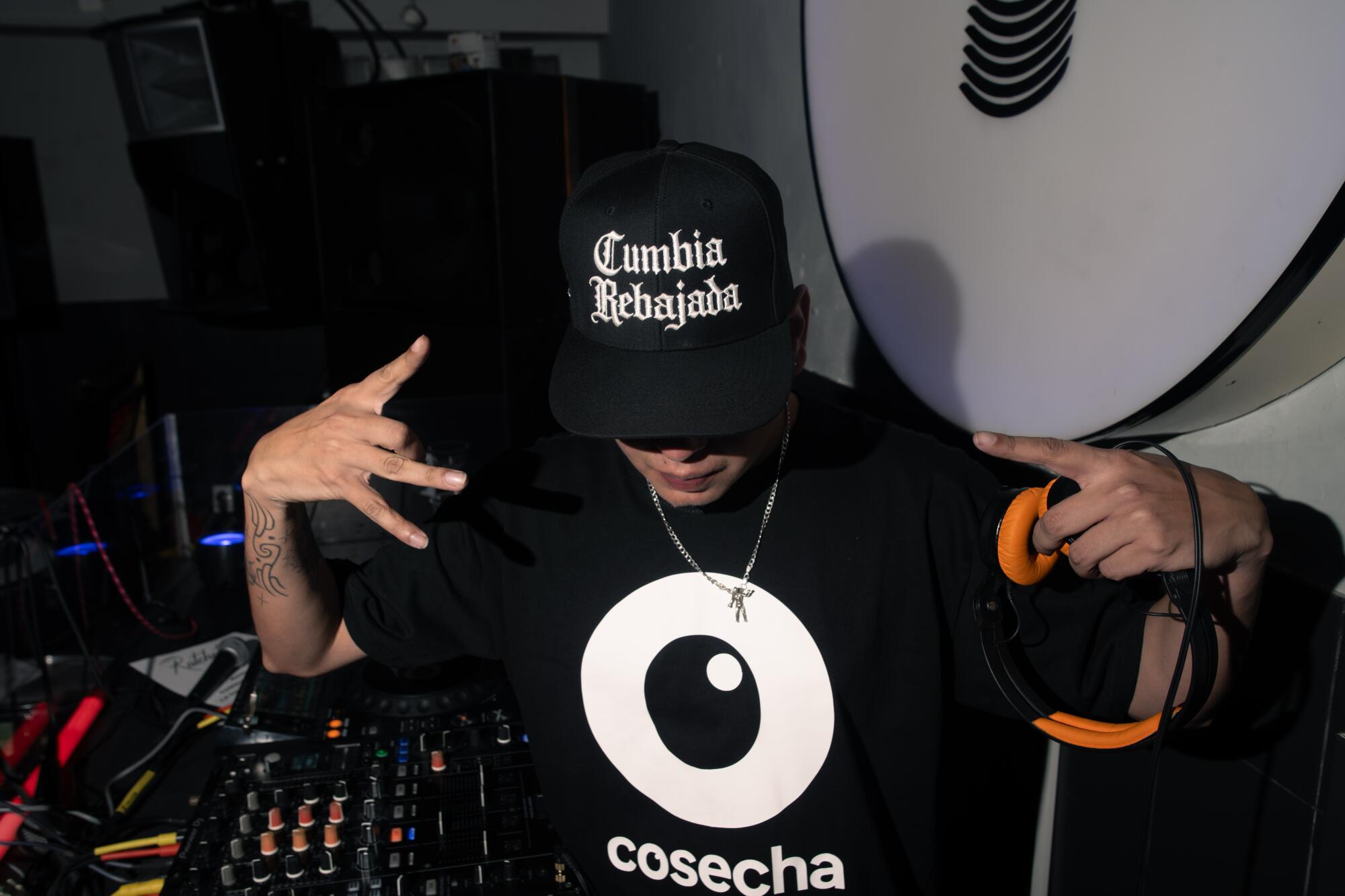 a dj poses for a portrait with their face covered by the brim of their cap