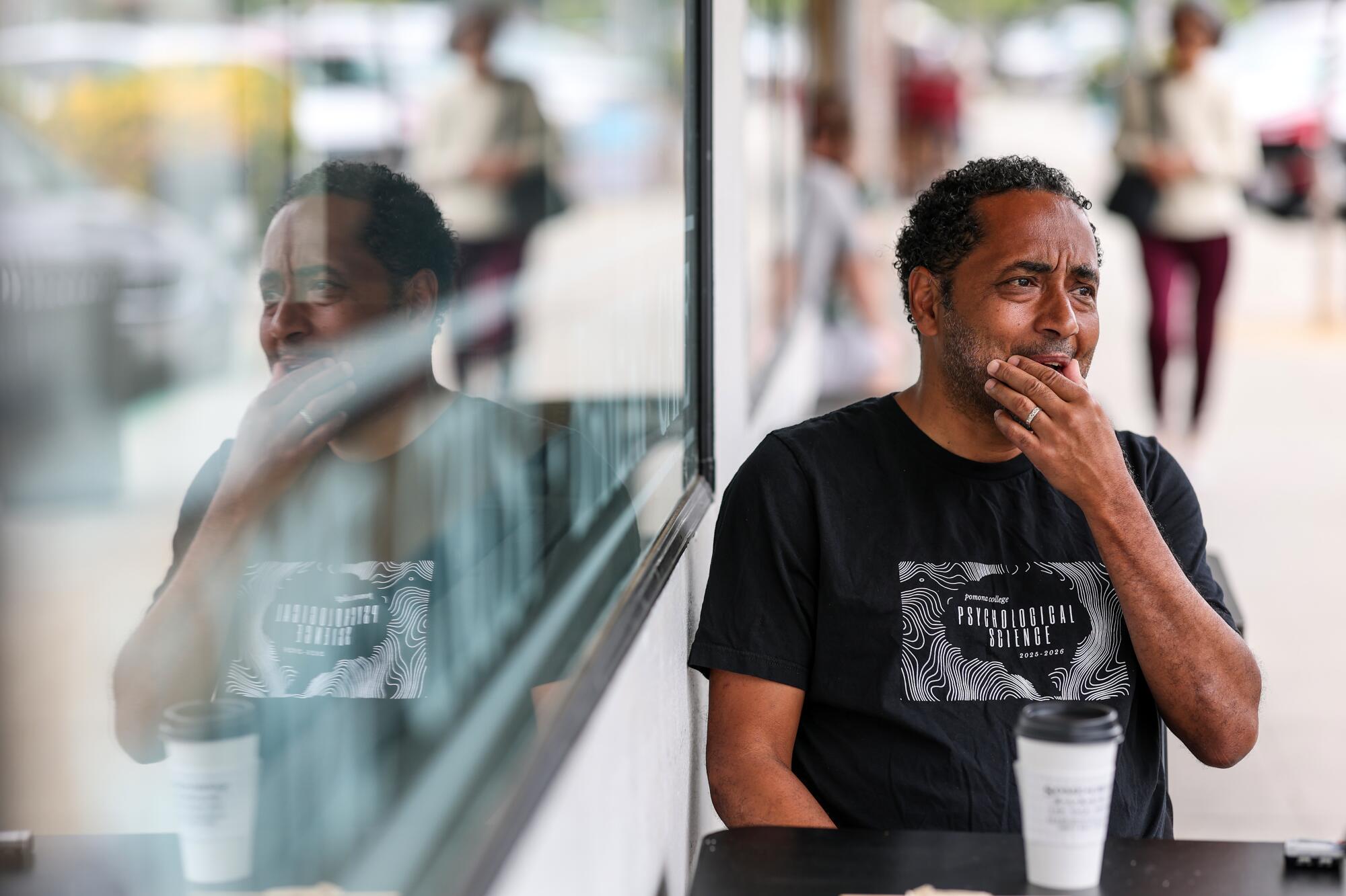 A man sitting outside a coffee shop with his image reflected in the window
