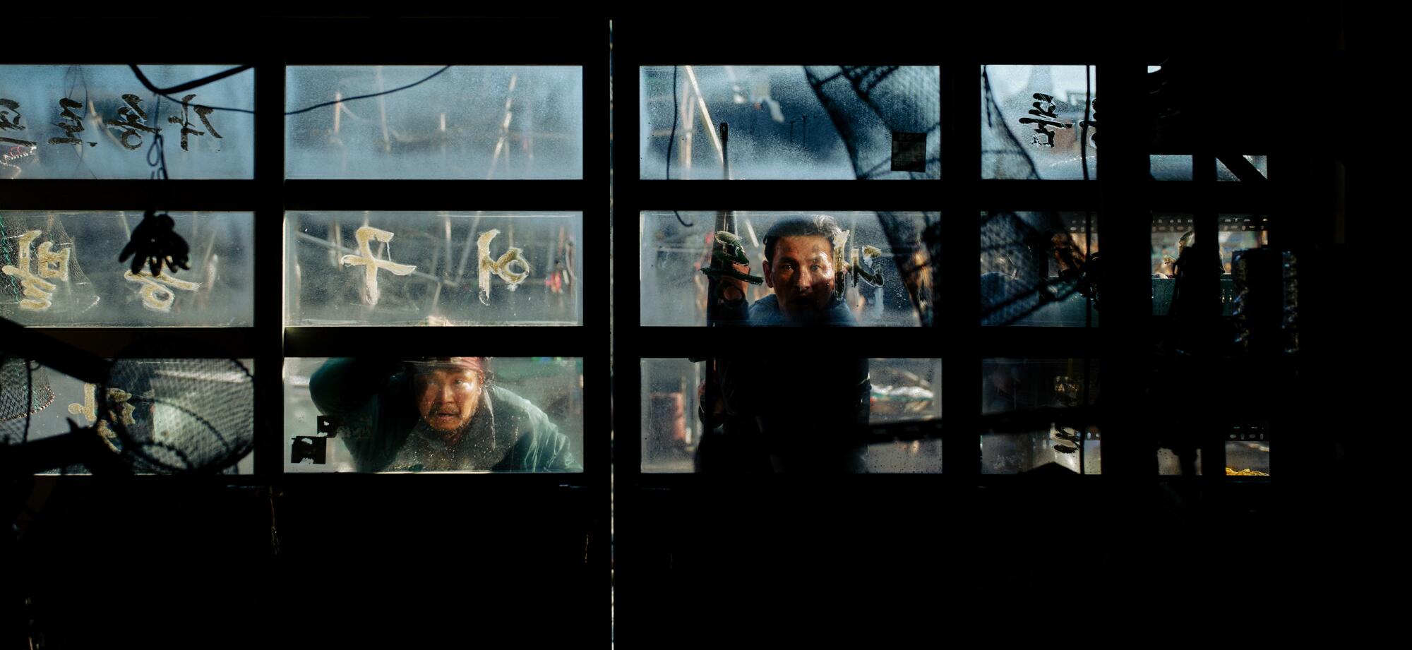 Two people peer through a window, nervously.