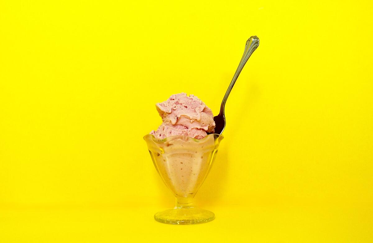 Strawberry ice cream in a glass goblet against a yellow backdrop.