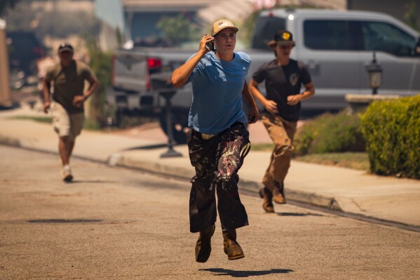 People run along a street as the Sandy Fire approaches a neighborhood Monday, May 18, 2026, in Simi Valley, Calif. (AP Photo/Ethan Swope)