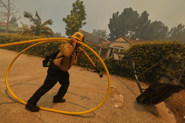 A firefighter sets up hoses while battling the Sandy Fire Monday, May 18, 2026, in Simi Valley, Calif. (AP Photo/Ethan Swope)