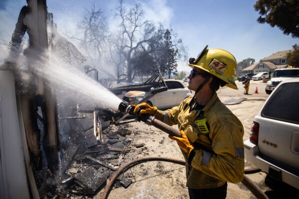 A firefighter hoses down hotspots at a property damaged by the Sandy Fire Monday, May 18, 2026, in Simi Valley, Calif. (AP Photo/Ethan Swope)