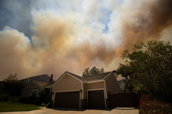 A man stands on a roof as the Sandy Fire approaches a neighborhood Monday, May 18, 2026, in Simi Valley, Calif. (AP Photo/Ethan Swope)