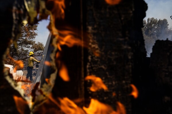 A firefighter hoses down hotspots at a property damaged by the Sandy Fire Monday, May 18, 2026, in Simi Valley, Calif. (AP Photo/Ethan Swope)