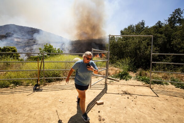 A woman steps away as the Sandy Fire approaches a neighborhood Monday, May 18, 2026, in Simi Valley, Calif. (AP Photo/Ethan Swope)