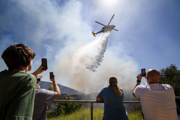 Onlookers watch as water is dropped onto the Sandy Fire Monday, May 18, 2026, in Simi Valley, Calif. (AP Photo/Ethan Swope)