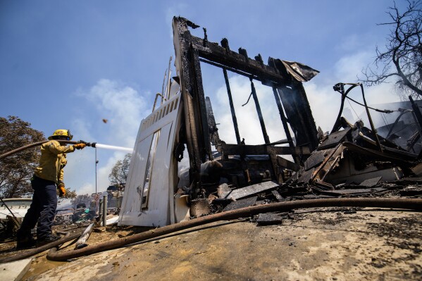 A firefighter hoses down hotspots at a property damaged by the Sandy Fire Monday, May 18, 2026, in Simi Valley, Calif. (AP Photo/Ethan Swope)