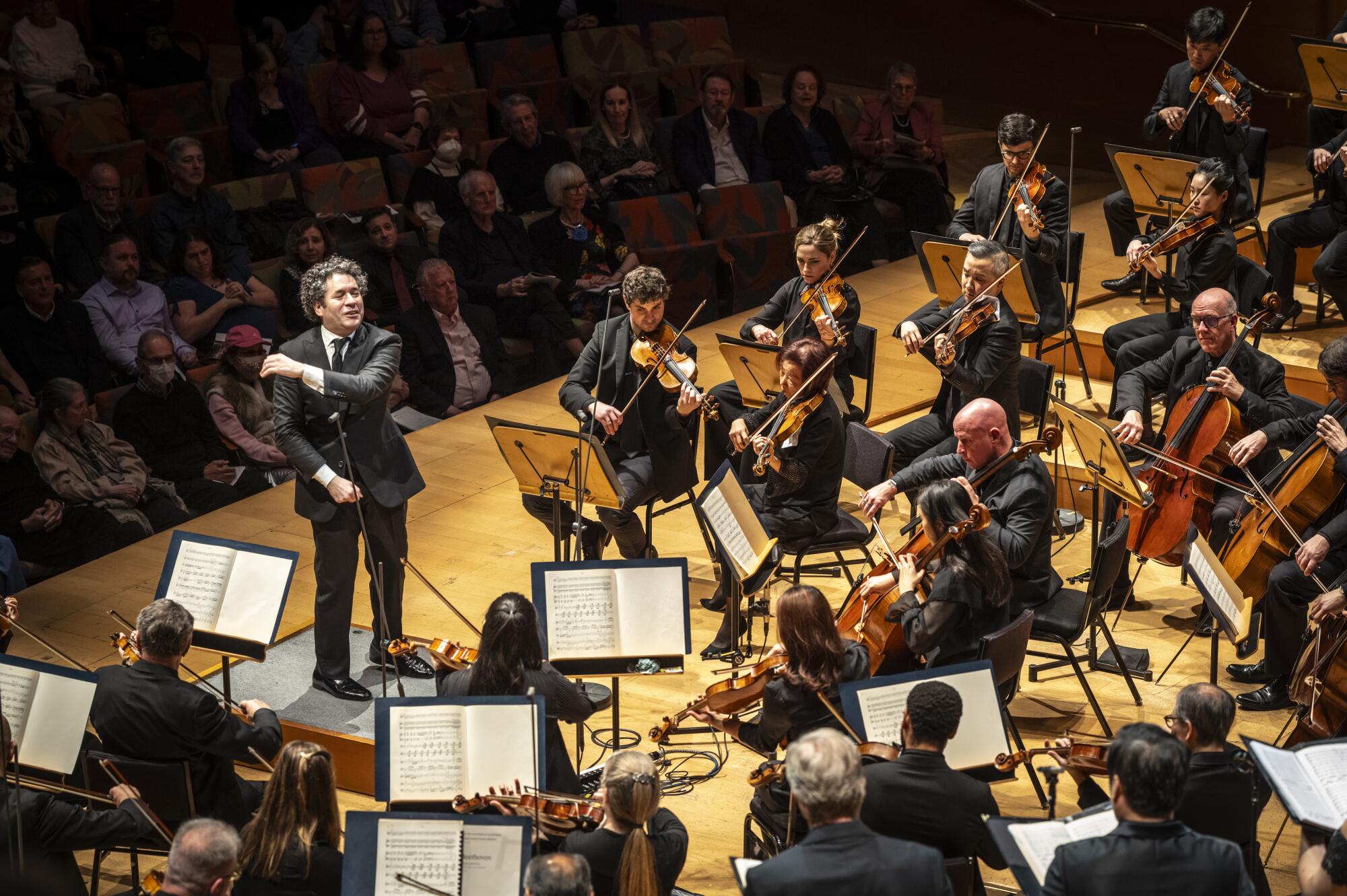 Gustavo Dudamel stands on stage with the L.A. Philharmonic orchestra.